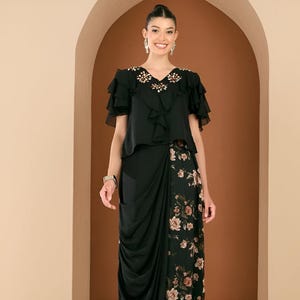 May include: A black formal outfit. The top has ruffled sleeves and floral embellishments at the neckline. The skirt features a draped design with a floral print panel. The outfit is completed with strappy heels, creating an elegant ensemble.