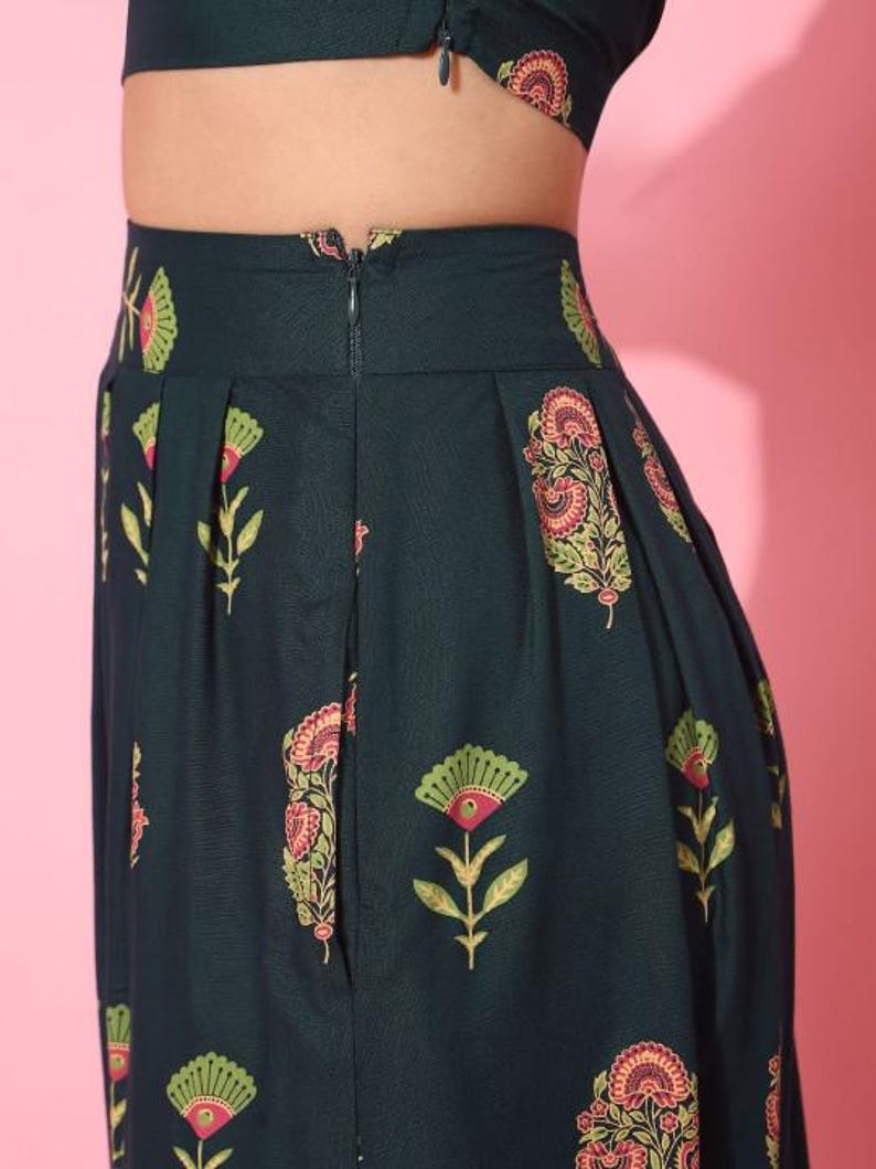May include: A dark green skirt with a floral print. The skirt has a zipper closure in the back and pleats in the front.