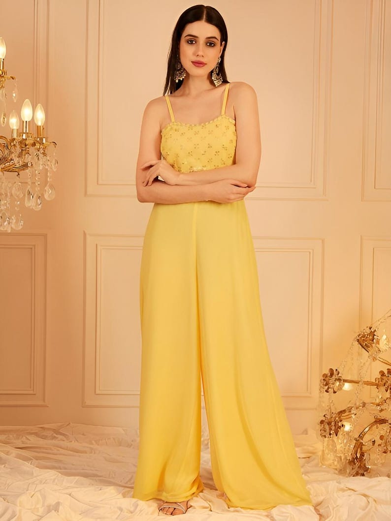 Pode incluir: Macac&atilde;o amarelo com corpete com contas e cal&ccedil;as de perna larga. A parte superior apresenta al&ccedil;as finas e um design detalhado. As cal&ccedil;as s&atilde;o de tecido liso e fluido. O traje &eacute; de cor brilhante e lisa.