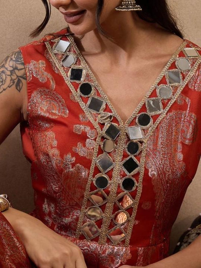 K&ouml;nnte beinhalten: Rotes &auml;rmelloses Kleid mit V-Ausschnitt. Der Ausschnitt ist mit Spiegeln und goldenen Verzierungen versehen. Das Kleid hat ein dezentes Blumenmuster und ein figurbetontes Oberteil.