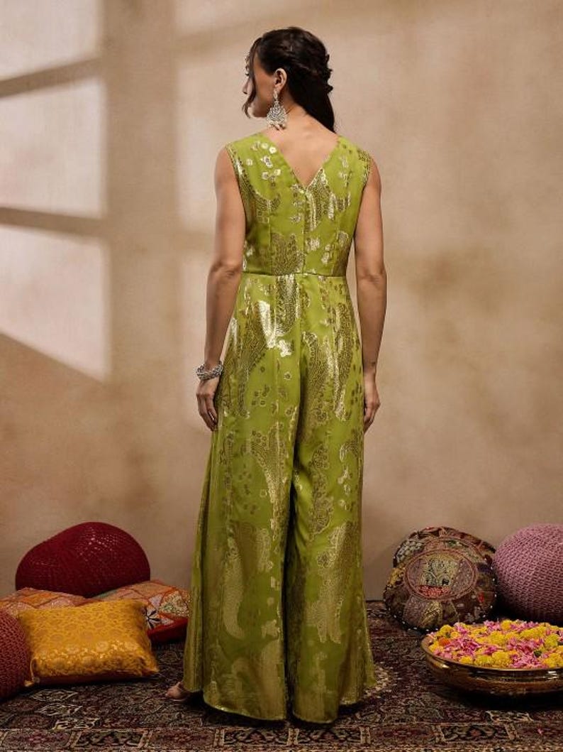 Op de afbeelding: Een groene jumpsuit met een gouden paisley print. De jumpsuit heeft een V-hals en is mouwloos. Het model draagt de jumpsuit en staat voor een beige achtergrond.