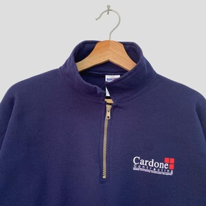 May include: A navy blue quarter-zip sweatshirt with a white logo that reads "Cardone Contracting" with a red square graphic.