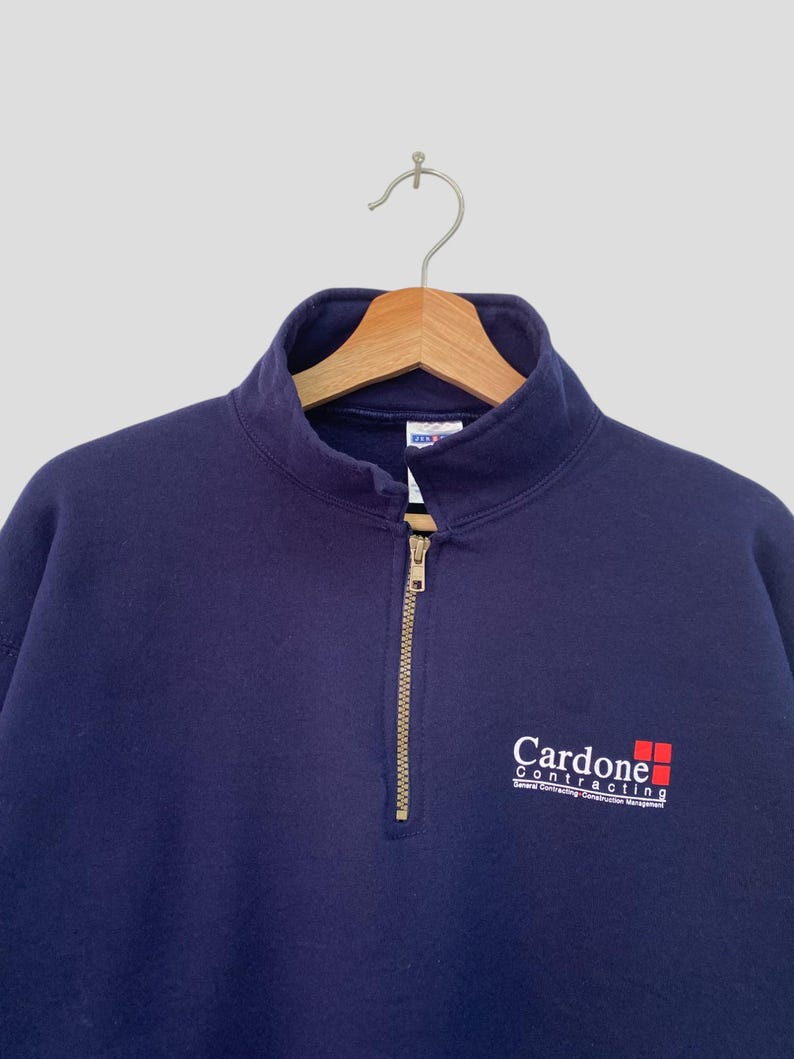 May include: A navy blue quarter-zip sweatshirt with a white logo that reads "Cardone Contracting" with a red square graphic.