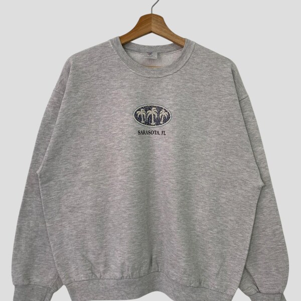 Könnte beinhalten: Ein grauer Pullover mit einem Palmenmotiv und dem Text "Sarasota, FL" in einem weißen Oval.