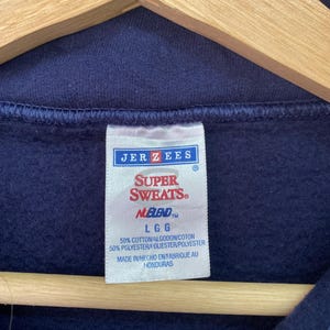 May include: A navy blue sweatshirt with a white tag that reads "JER ZEES SUPER SWEATS NEBLEND LGG 50% COTTON/ALGODON/COTON 50% POLYESTER/POLIESTER/POLYESTER MADE IN HECHO EN FABRIQUE AU HONDURAS".