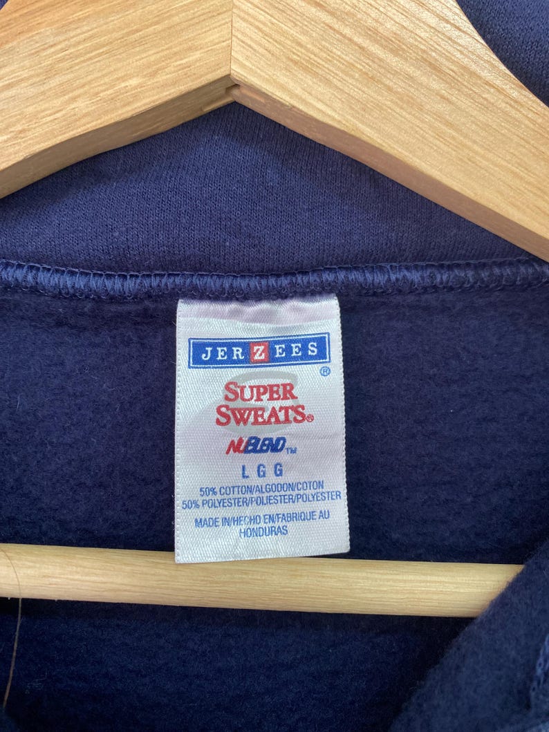 May include: A navy blue sweatshirt with a white tag that reads "JER ZEES SUPER SWEATS NEBLEND LGG 50% COTTON/ALGODON/COTON 50% POLYESTER/POLIESTER/POLYESTER MADE IN HECHO EN FABRIQUE AU HONDURAS".