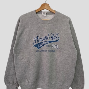 May include: Grey sweatshirt with a blue and white graphic print that reads "Pleasant Hill California Inc. 1961 An American Original".