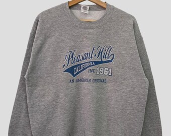 Puede incluir: Sudadera gris con un estampado gráfico azul y blanco que dice "Pleasant Hill California Inc. 1961 An American Original".