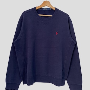 May include: A navy blue sweatshirt with a small red polo player logo on the chest. The sweatshirt has a crew neck and long sleeves.