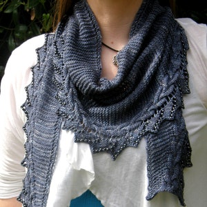 May include: A gray knitted scarf with a beaded edge. The scarf is draped around a person's neck and shoulders.