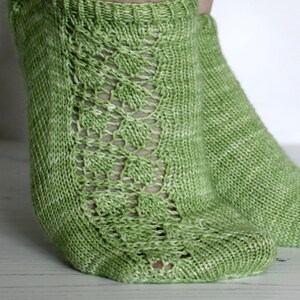 May include: A pair of green knitted socks with a decorative openwork pattern on the sides. The socks are a light green color with a textured appearance, and the openwork design adds a delicate touch.