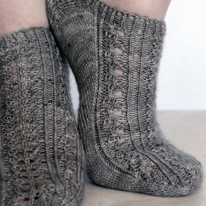 May include: Close-up of two gray knitted socks. The socks have a textured pattern with vertical ribbing and decorative openwork details. The socks are made of a soft, warm material, perfect for cold weather.