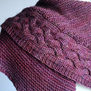 May include: A close-up of a knitted scarf with a cable knit pattern in shades of purple and pink.
