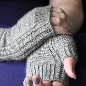 May include: A pair of gray knitted fingerless gloves with a ribbed texture. The gloves are folded over the hands of a person wearing them.