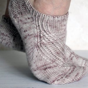 May include: Knitted ankle socks in light grey and burgundy. The socks have an openwork design on the top of the foot and a ribbed cuff. The socks are made of a soft, textured yarn. The socks are designed to be worn on the feet.