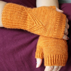 Puede incluir: Un par de guantes sin dedos de color naranja con un patrón de punto texturizado. Los guantes están hechos de un material suave y cálido, perfectos para mantener las manos calientes en invierno.