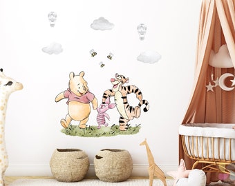 May include: Winnie the Pooh, Piglet, and Tigger wall decals in a watercolor style. The characters are walking and holding hands. There are also clouds, hot air balloons, and bees in the design.