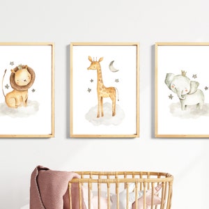 May include: Three framed watercolor prints featuring a lion, giraffe, and elephant wearing crowns and standing on clouds with stars. The prints are set against a white wall.