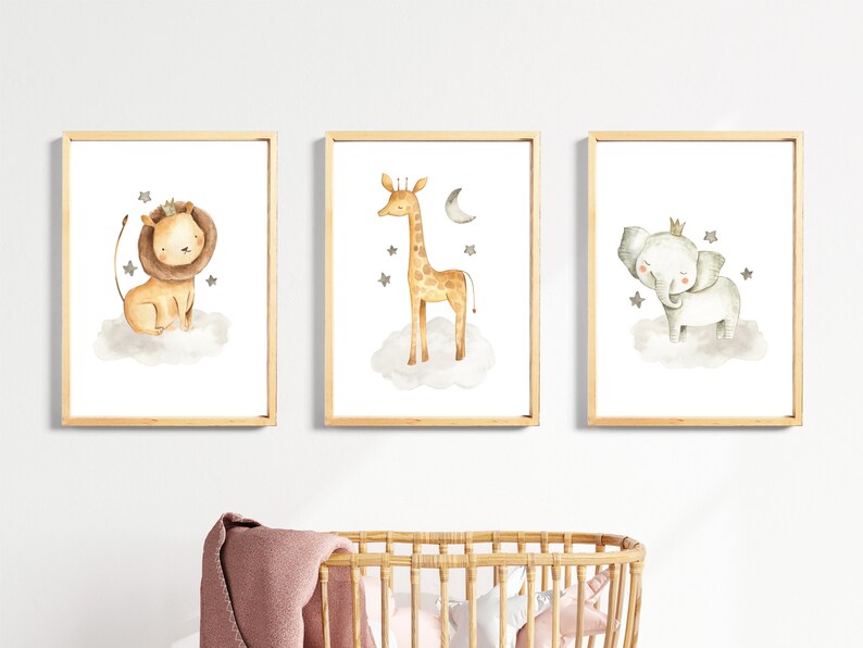 May include: Three framed watercolor prints featuring a lion, giraffe, and elephant wearing crowns and standing on clouds with stars. The prints are set against a white wall.