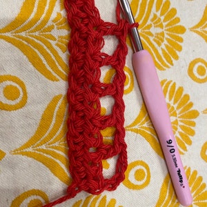 May include: Close-up of red crochet fabric being worked on with a pink crochet hook labeled "9/0 5.50MM Tulip".