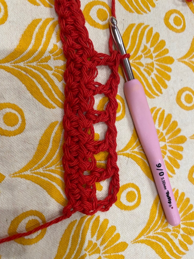 May include: Close-up of red crochet fabric being worked on with a pink crochet hook labeled "9/0 5.50MM Tulip".