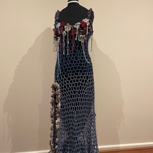 May include: A long, blue crochet dress with a floral design on the bodice. The dress has a loose, flowing fit and a scalloped hem.