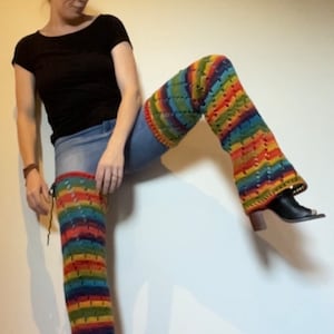 Puede incluir: Una persona con una camisa negra y pantalones vaqueros azules con polainas de crochet a rayas de arco&iacute;ris.