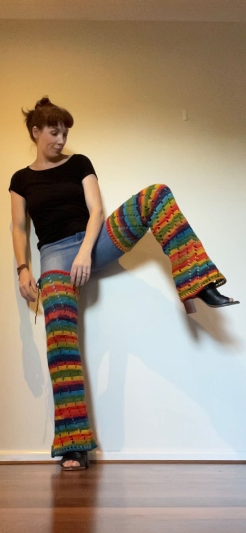 Puede incluir: Una persona con una camisa negra y pantalones vaqueros azules con polainas de crochet a rayas de arco&iacute;ris.