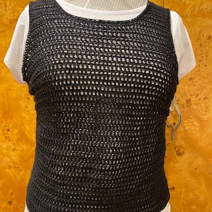 May include: Black crochet top with a mesh design. The top is sleeveless and has a round neckline.