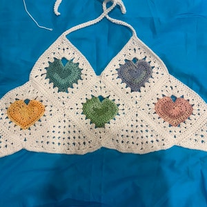 Puede incluir: Top de halter blanco de crochet con un patrón geométrico de corazones coloridos. Los corazones son en tonos de verde, azul, rosa y amarillo.