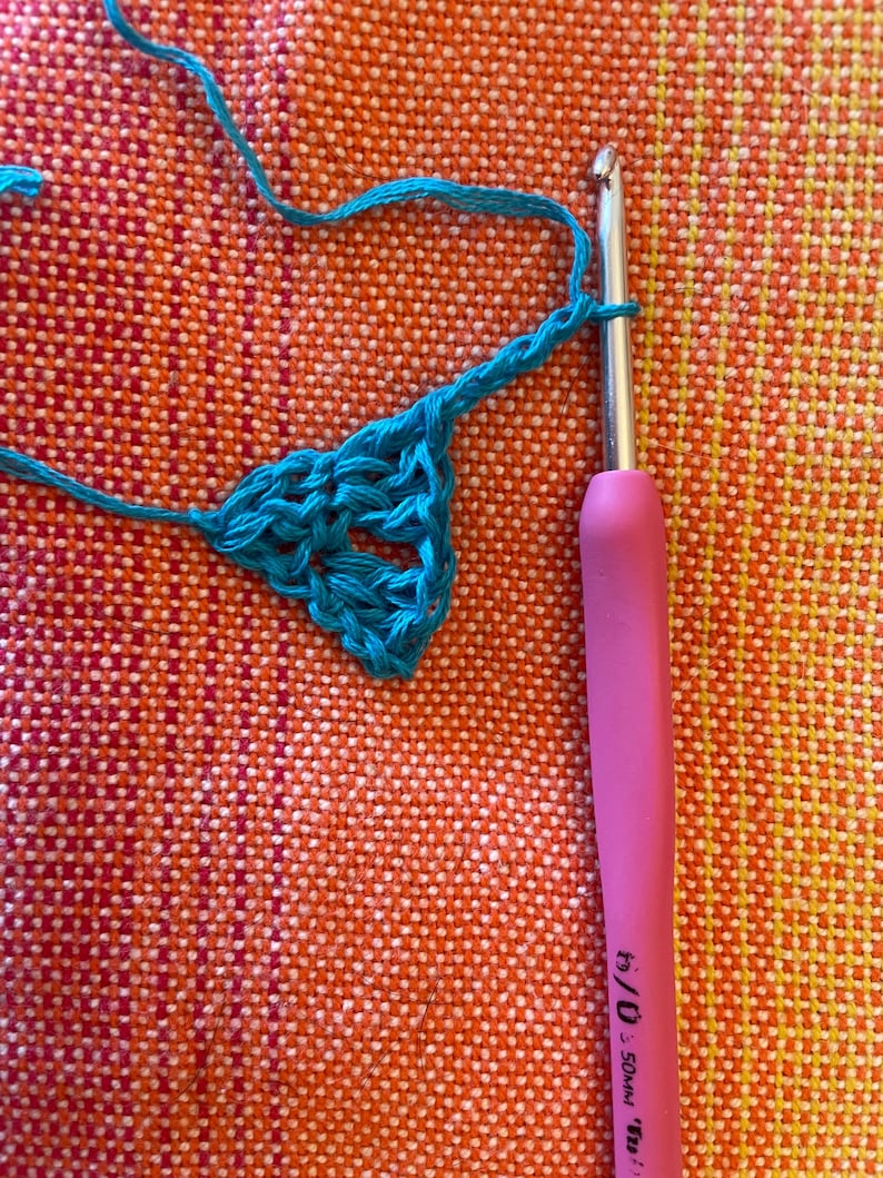 May include: A close-up of a turquoise crochet project in progress. A pink crochet hook with the text "5.0 mm" is visible in the image.