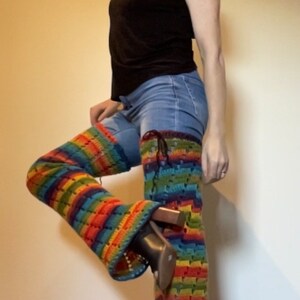Puede incluir: Una persona que lleva una camisa negra y pantalones vaqueros azules con polainas de crochet arco&iacute;ris y zapatos negros de tac&oacute;n.