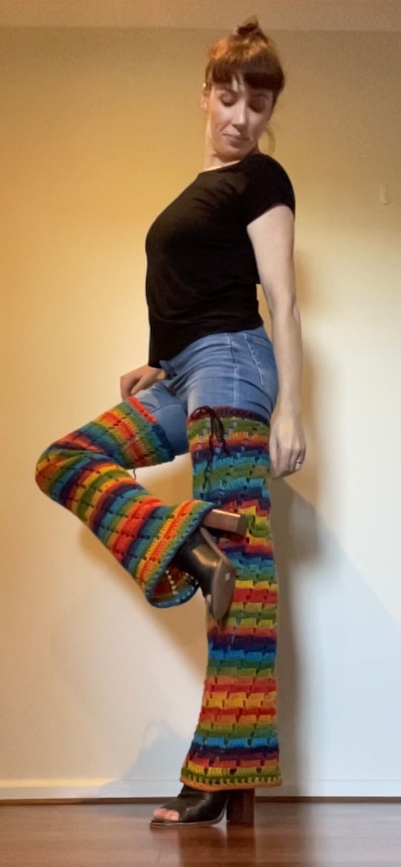 Puede incluir: Una persona que lleva una camisa negra y pantalones vaqueros azules con polainas de crochet arco&iacute;ris y zapatos negros de tac&oacute;n.