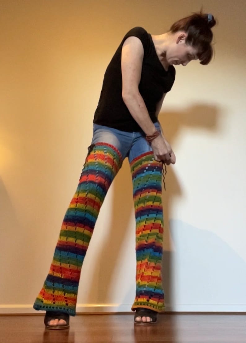 Puede incluir: Una persona lleva puestas unas polainas de crochet de arco&iacute;ris sobre unos vaqueros azules. Las polainas est&aacute;n hechas con un hilo de colores y tienen un patr&oacute;n de encaje.