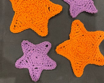 May include: Four crocheted star-shaped coasters, two orange and two purple.