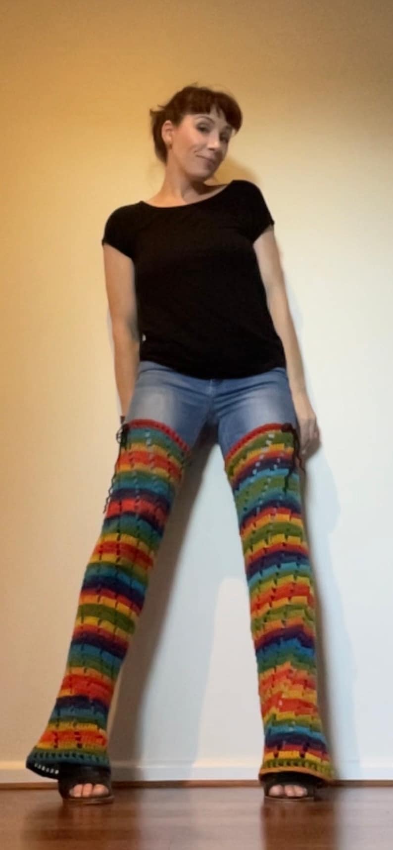 Puede incluir: Una persona con una camisa negra y pantalones vaqueros azules con polainas de crochet de arco&iacute;ris.