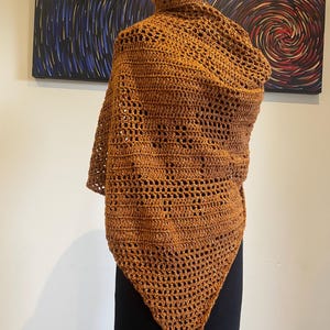 May include: A brown crocheted shawl with a triangular shape and a lacy pattern.