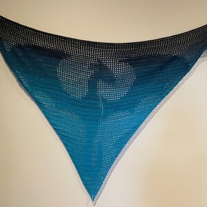 May include: A triangular crocheted shawl with a gradient of blue and black colors. The shawl is made with a delicate openwork stitch.