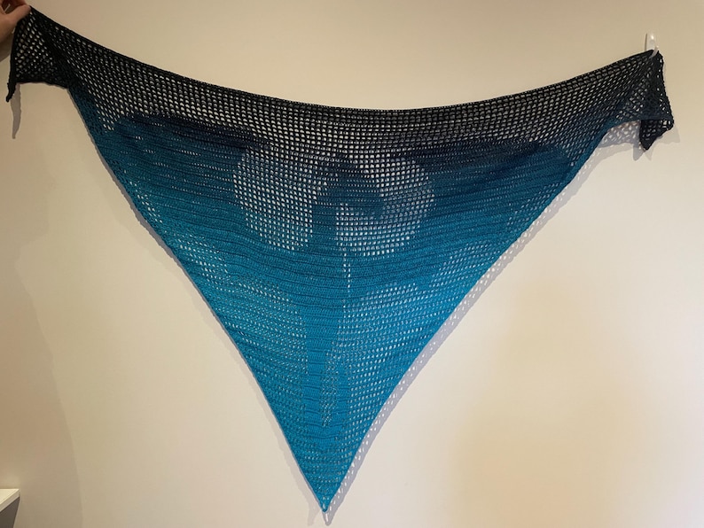 May include: A triangular crocheted shawl with a gradient of blue and black colors. The shawl is made with a delicate openwork stitch.