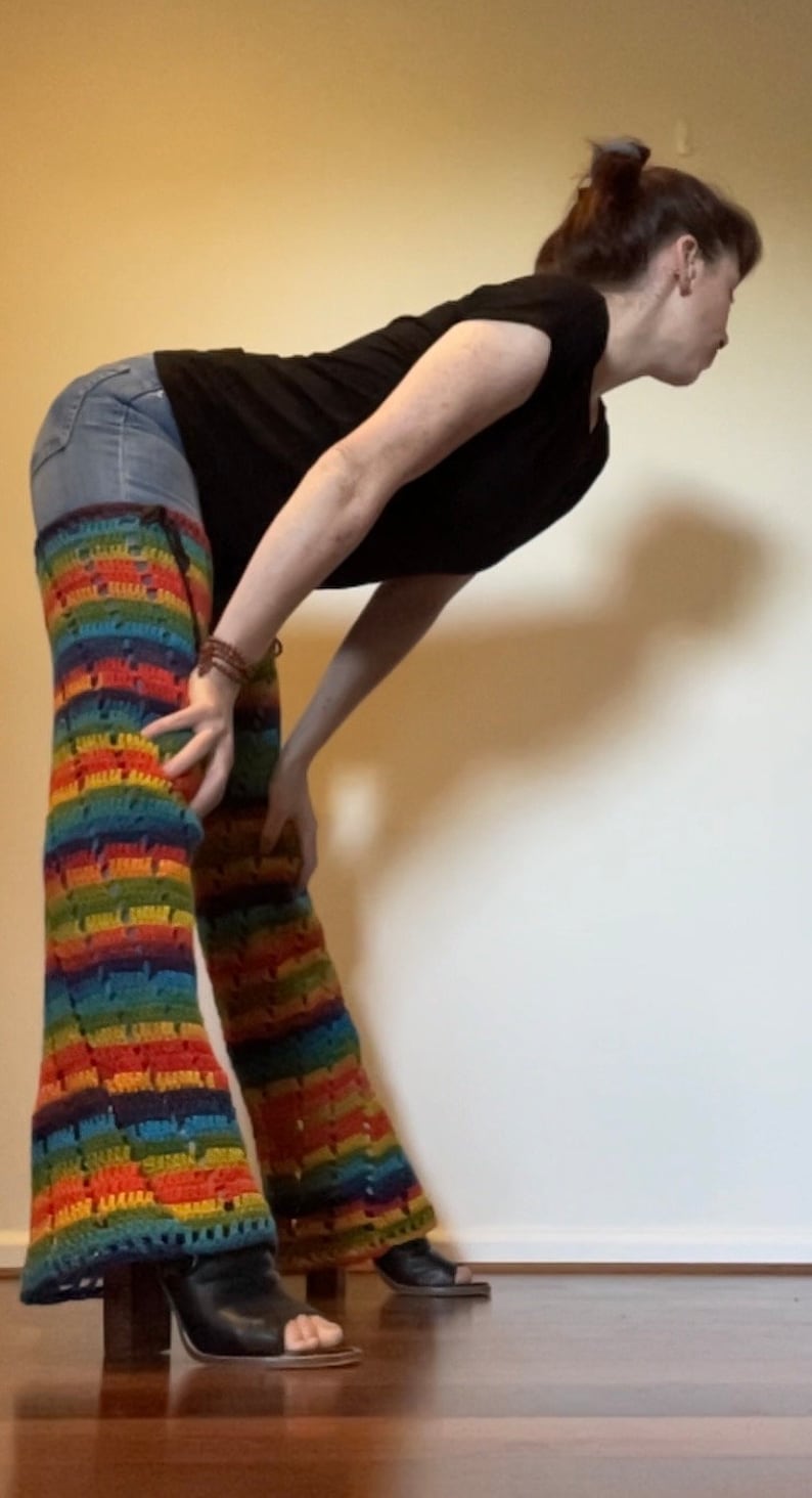 Puede incluir: Una persona con una camisa negra y pantalones vaqueros azules con polainas de crochet arco&iacute;ris.