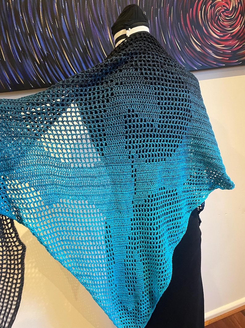 May include: A teal and black crochet shawl with a lacy pattern. The shawl is draped over a mannequin.