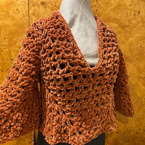 May include: A brown crocheted sweater with a loose fit and bell sleeves. The sweater is made of a soft, fuzzy yarn.
