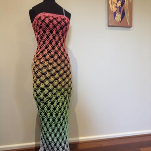 May include: A long, rainbow crochet dress with a delicate, open-weave pattern. The dress is sleeveless and has a halter neckline.