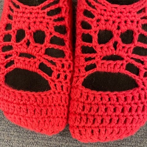 May include: A pair of red crocheted slippers with a black fabric lining. The slippers have a unique openwork design.