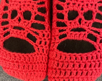 May include: A pair of red crocheted slippers with a black fabric lining. The slippers have a unique openwork design.