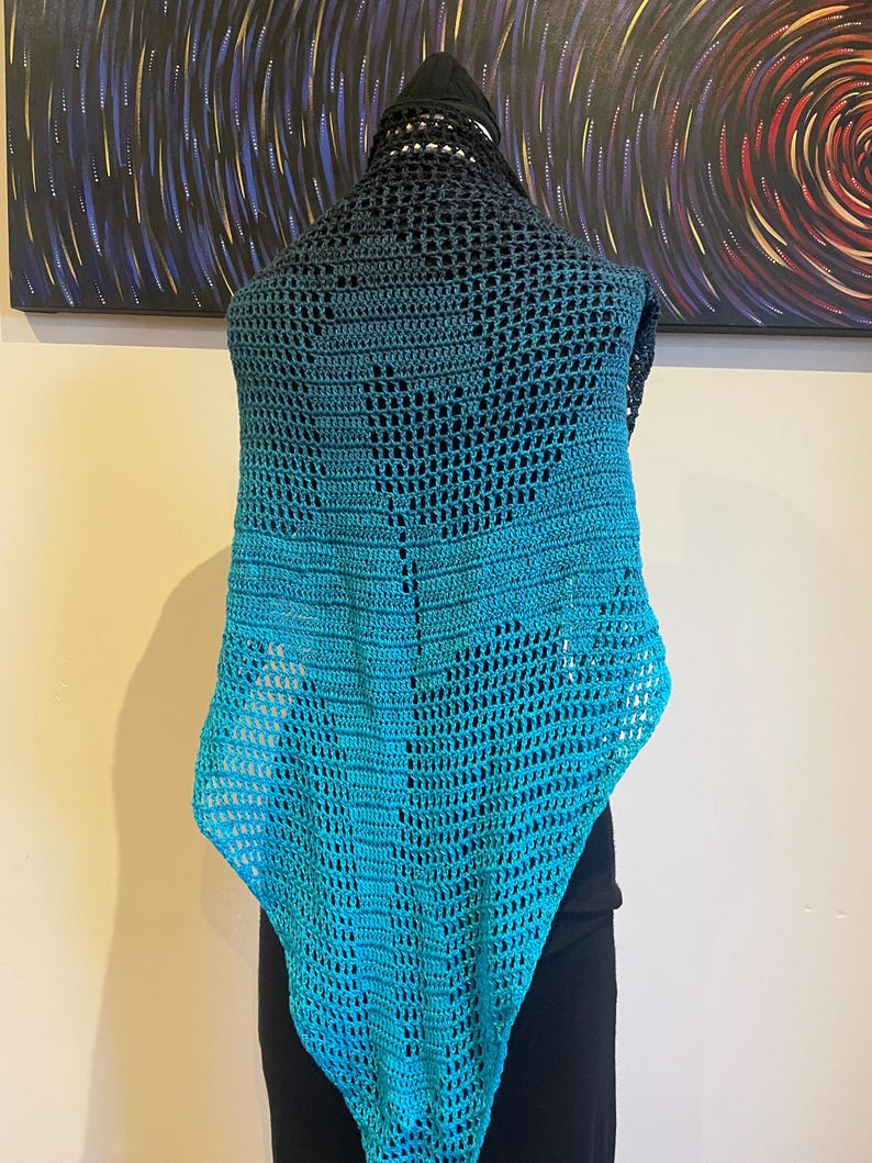 May include: A teal and black crochet shawl with a lacy pattern. The shawl is draped over a mannequin.