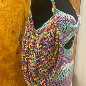 May include: A colorful crocheted mesh bag with a rainbow pattern. The bag is hanging on a mannequin wearing a crocheted dress.