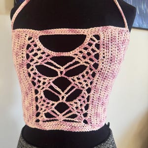 Puede incluir: Top halter de ganchillo hecho a mano en tonos rosa y crema. El top presenta un diseño calado único en la parte delantera, con cuello halter y una silueta ajustada. El hilo tiene un sutil efecto de color variado.