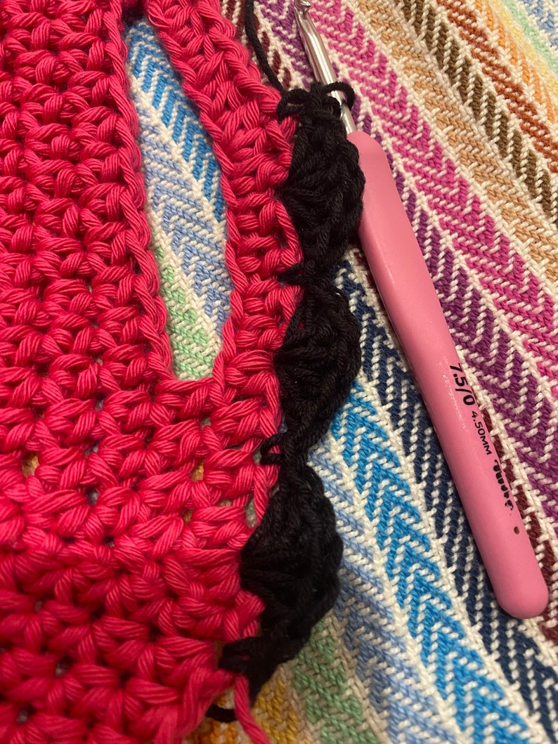 May include: Close-up of a pink crochet hook with a black crochet border on a pink and black striped fabric.