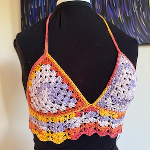 May include: A crocheted halter top with a multi-colored design. The top is made with a variety of shades of purple, orange, and yellow yarn.